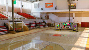 indoor gym with red and white bleachers basketball hoop and a large color test pattern display on the court center youprotv youprotv