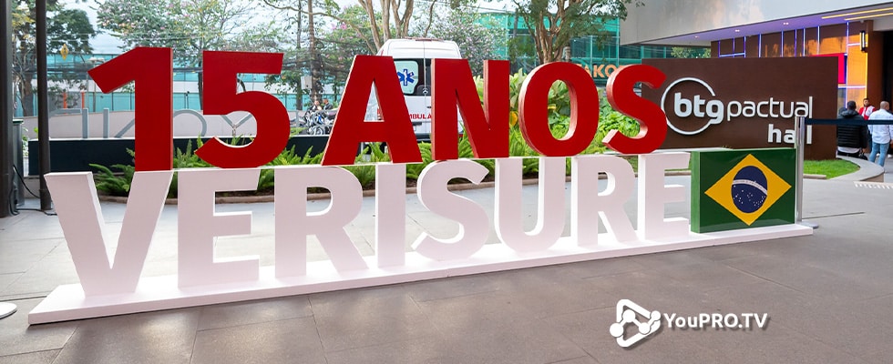 large outdoor sign reading 15 anos verisure with a brazilian flag and youprotv watermark in a public plaza  youprotv